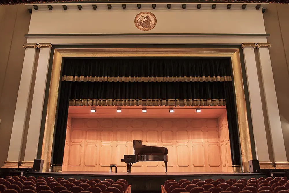Vista general del escenario en el que hay un piano como escenografía, y la segunda fotografia es el medallón del teatro Filarmónica